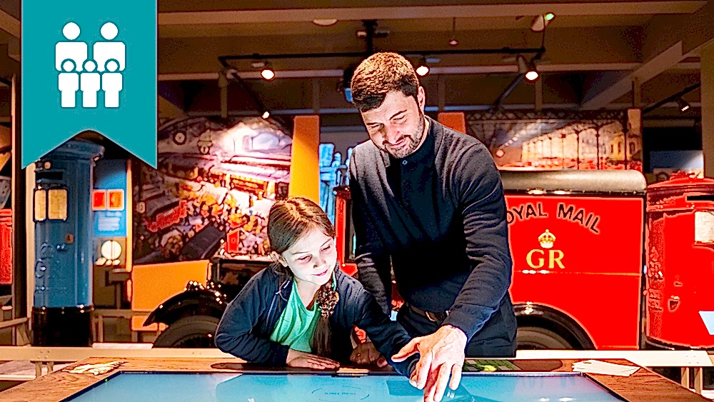 A parent and child exploring the touch table in The Postal Museum exhibition space.