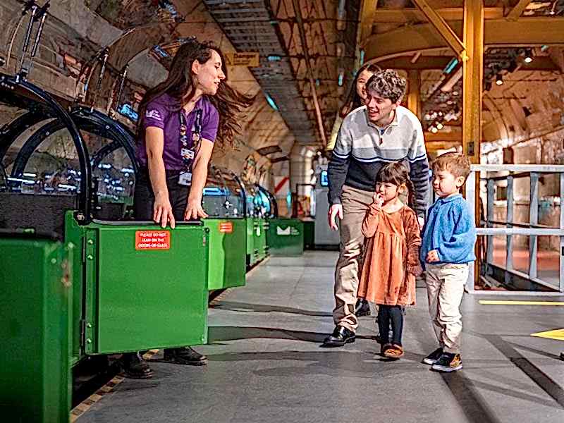 A family waiting to board the green miniature Mail Rail train at The Postal Museum.