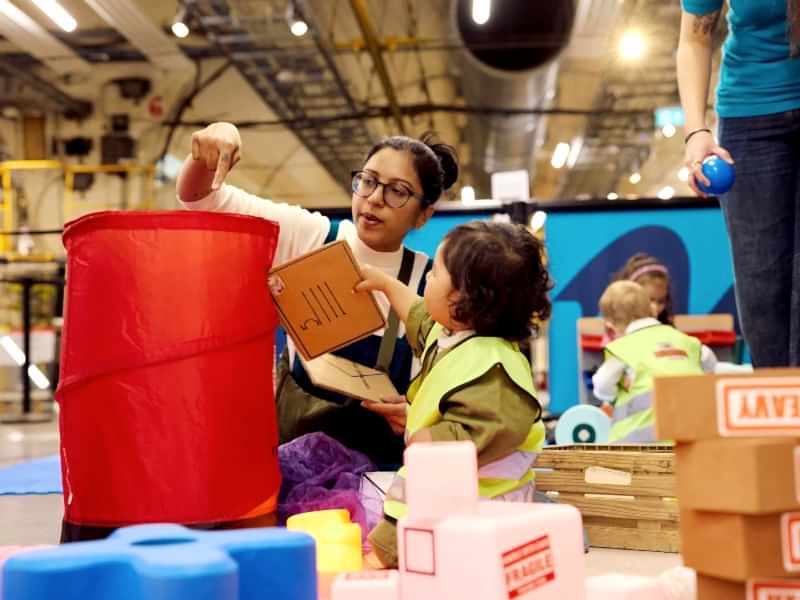 A young boy hands his mum a cardboard envelope to 'post' in a popup red Post Box.