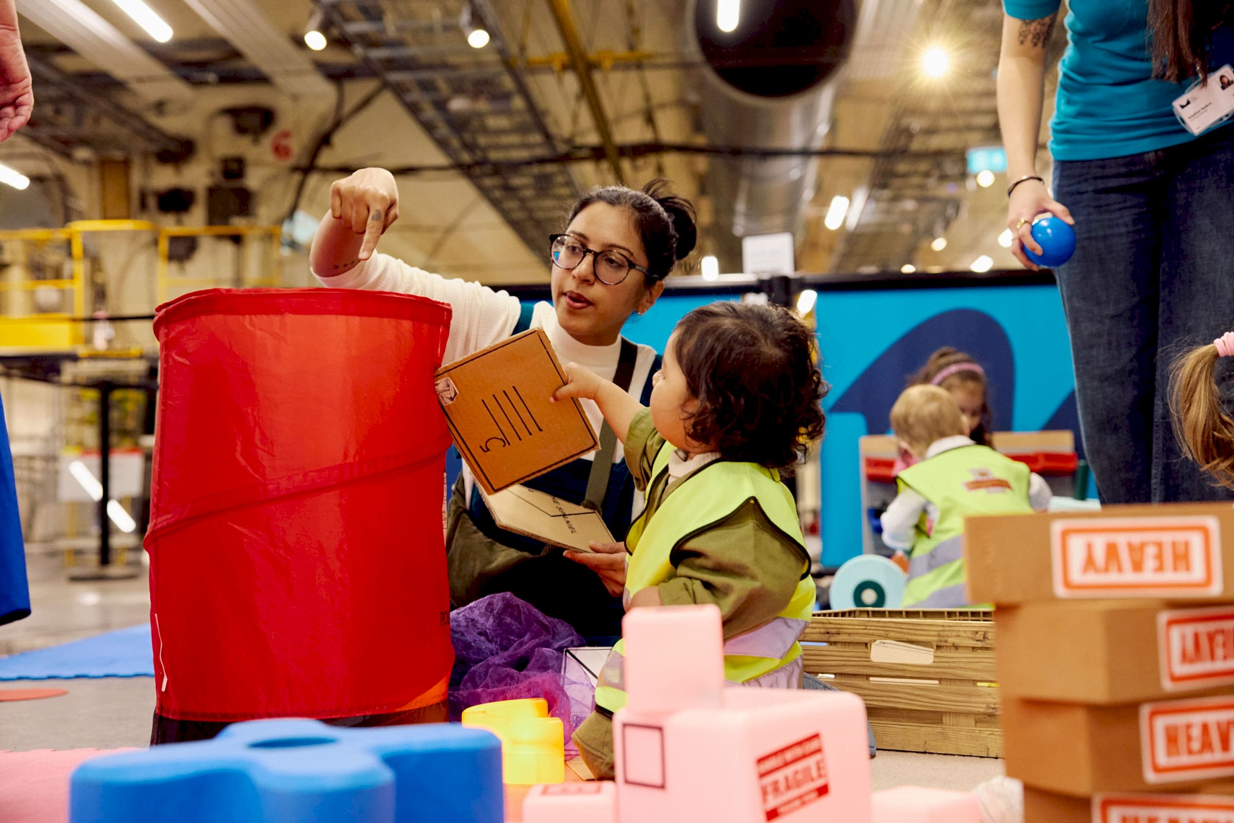 A young boy hands his mum a cardboard envelope to 'post' in a popup red Post Box.