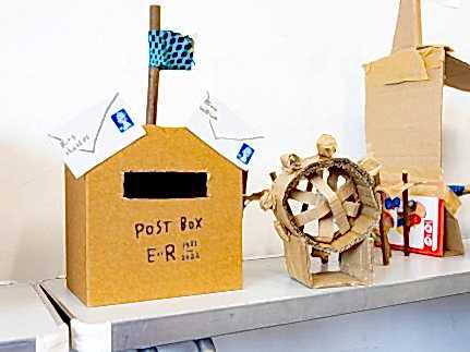 A cardboard postbox and wheel on a craft table.