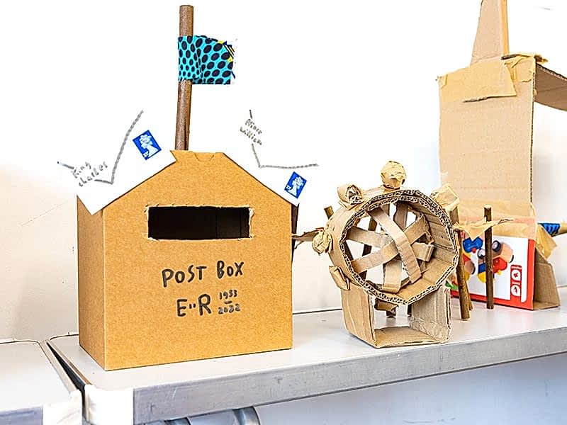 A cardboard postbox and wheel on a craft table.