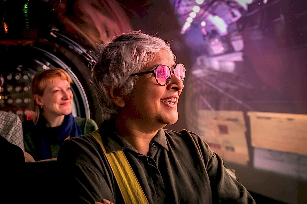 Women riding a miniature train, looking out at a projected display in the tunnels.